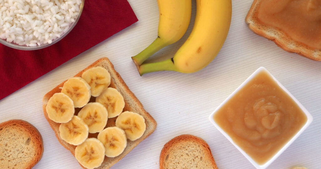 Foods included in the BRAT diet: bananas, rice, applesauce, toast. Food to consume while diarrhea or stomach virus. Flat lay.
