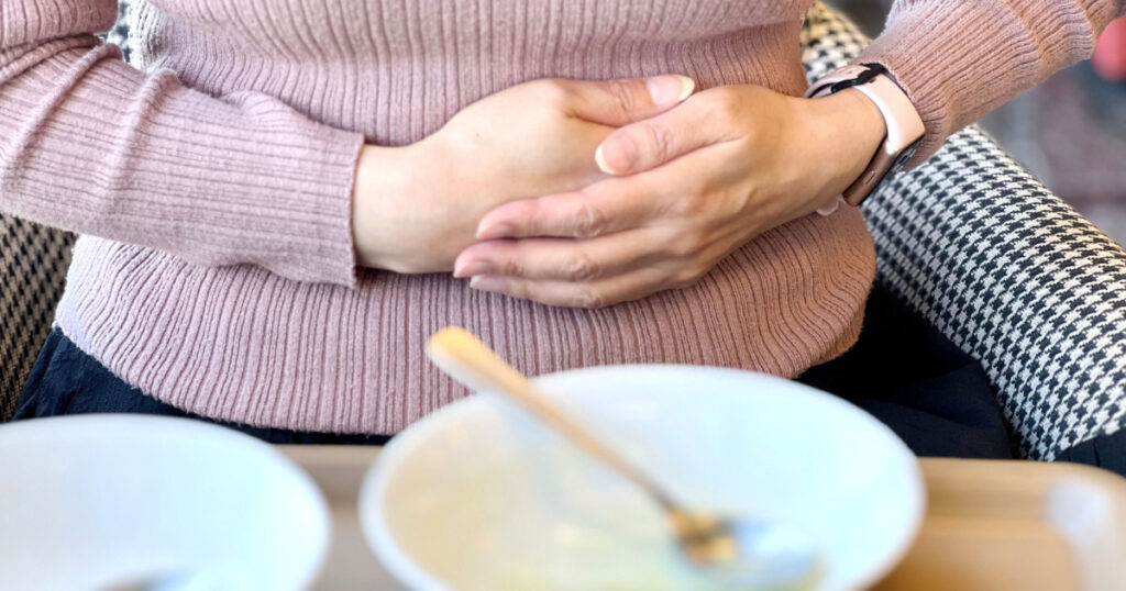 A woman holding her stomach with both hands in front of the finished plate
