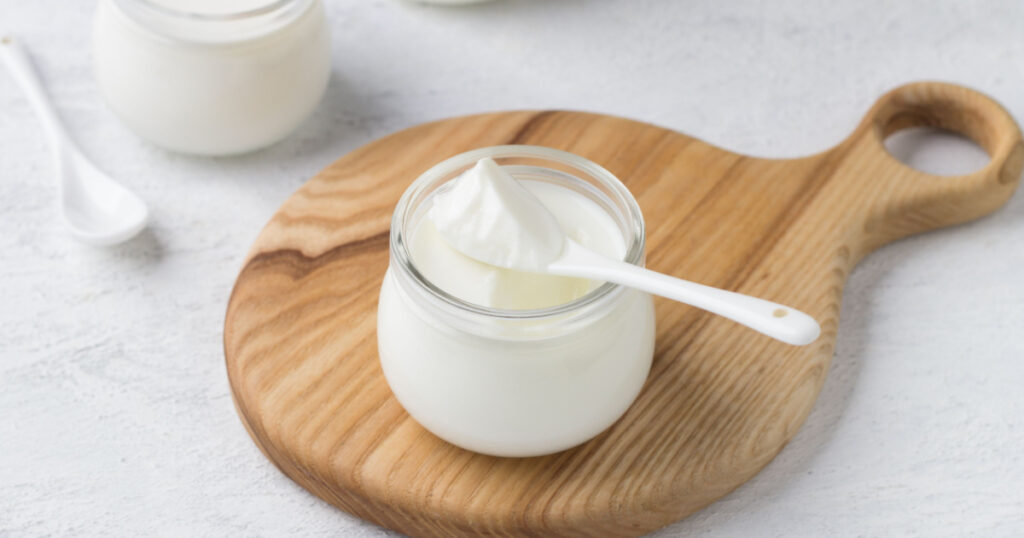 Natural homemade yogurt in a glass jar on a wooden board on a light gray background