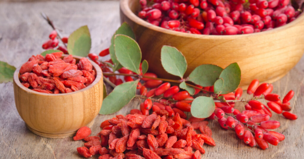 Barberry and dry goji berries in bowls on wooden background