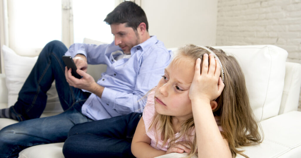 young internet addict father using mobile phone ignoring his little sad daughter looking bored lonely and depressed feeling abandoned and disappointed with her dad in parent bad selfish behavior