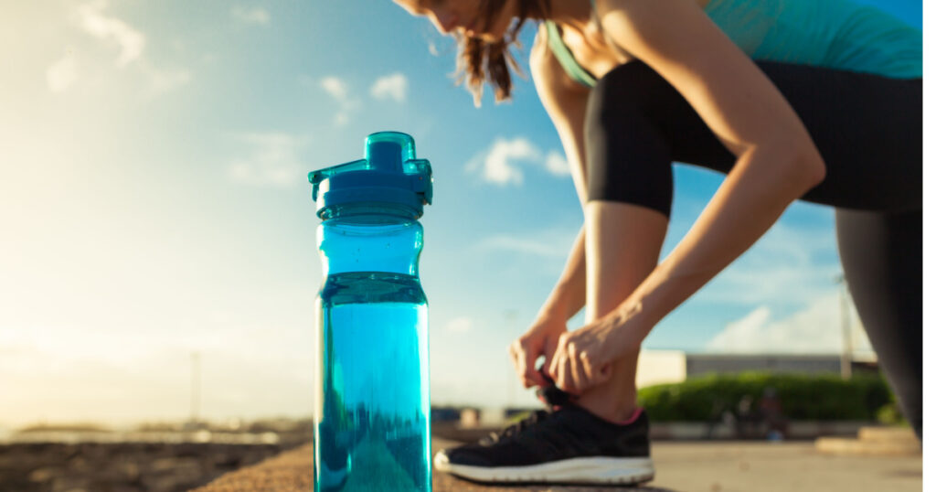 Drinking water concept. Female runner tying her shoe next to bottle of water.