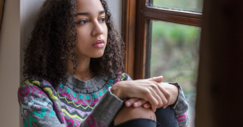 Beautiful mixed race biracial African American girl teenager female young woman sad depressed or thoughtful looking out of a window
