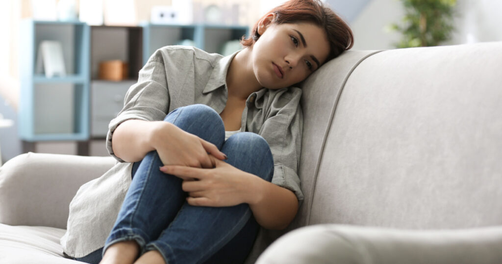 Depressed young woman sitting on sofa at home
