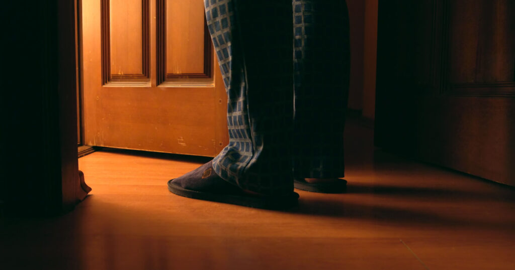 Adult man stands near door to a bathroom at the night
