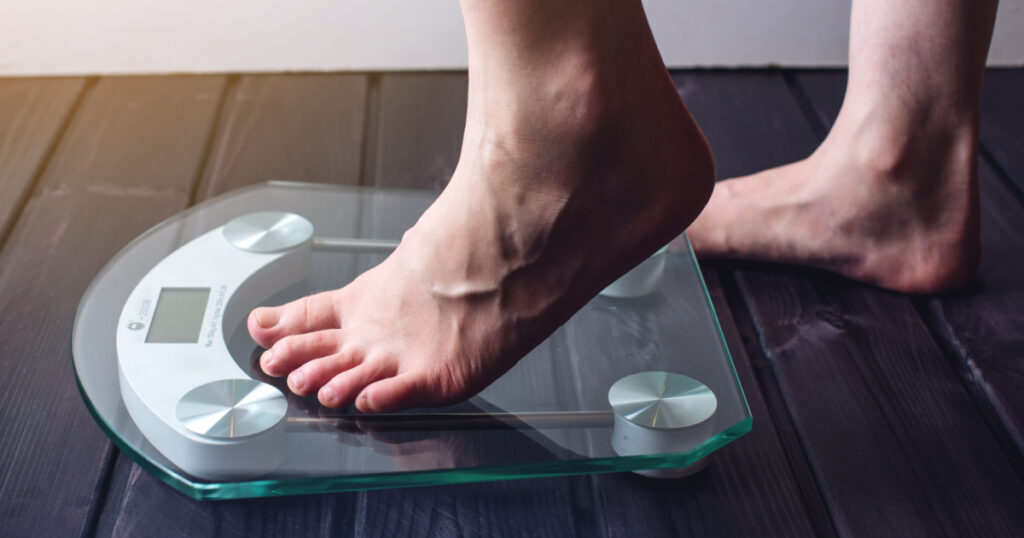 Female feet standing on electronic scales for weight control on wooden background. The concept of slimming and weight loss
