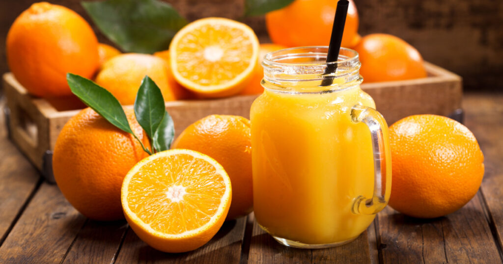glass jar of fresh orange juice with fresh fruits on wooden table

