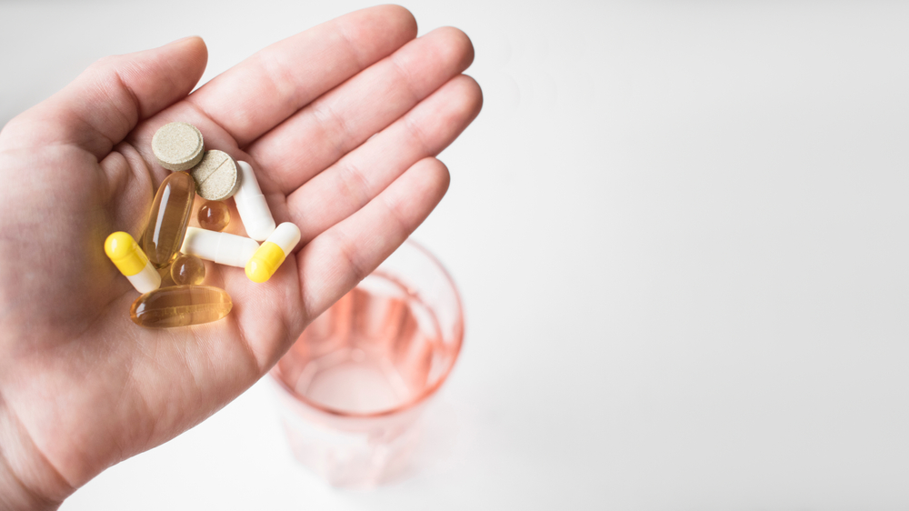 Female hand holds Dietary Supplements and Vitamins: Omega 3, Magnesium and Calcium and Ferrum, Vitamin D, Biotin on background glass of water.