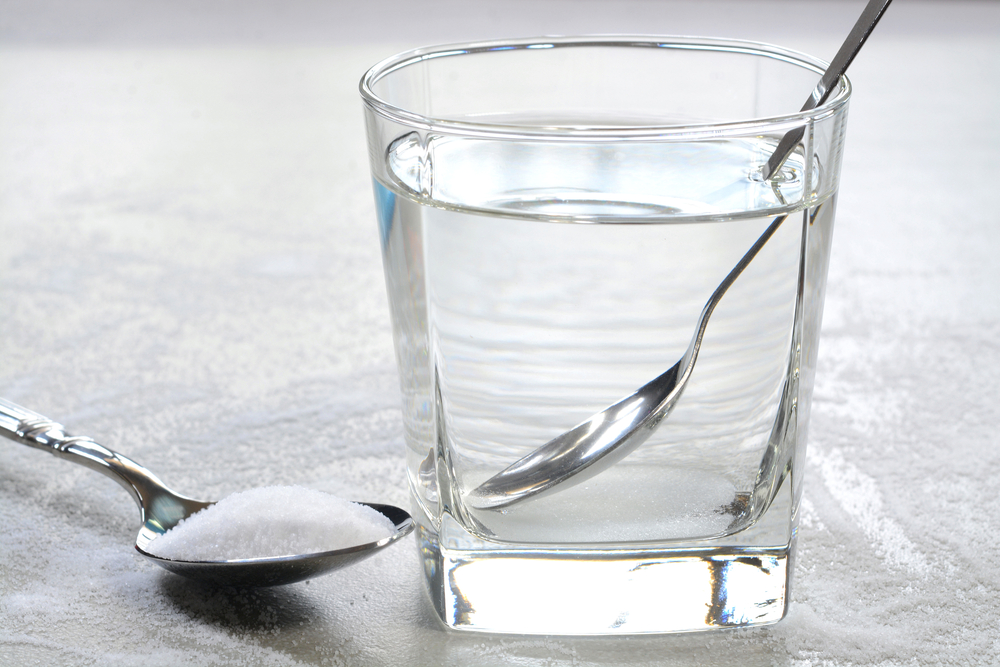 Salt water in a glass cup and salt in a teaspoon. Salt water has high level of minerals and salt water gargle helps in removing of cold and sore throat
