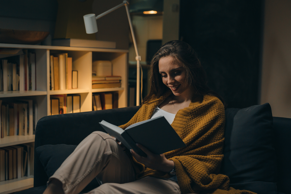woman relaxing on sofa and reading book. evening moody ambience. she is enjoying time during weekend
