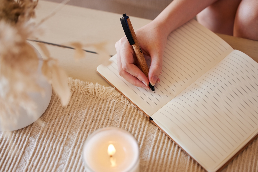 Hand, candle and woman writing in journal with top view for calm, peace mindset and relax morning routine in home. Hands, notebook and diary planning goals, idea vision or creative writer lifestyle