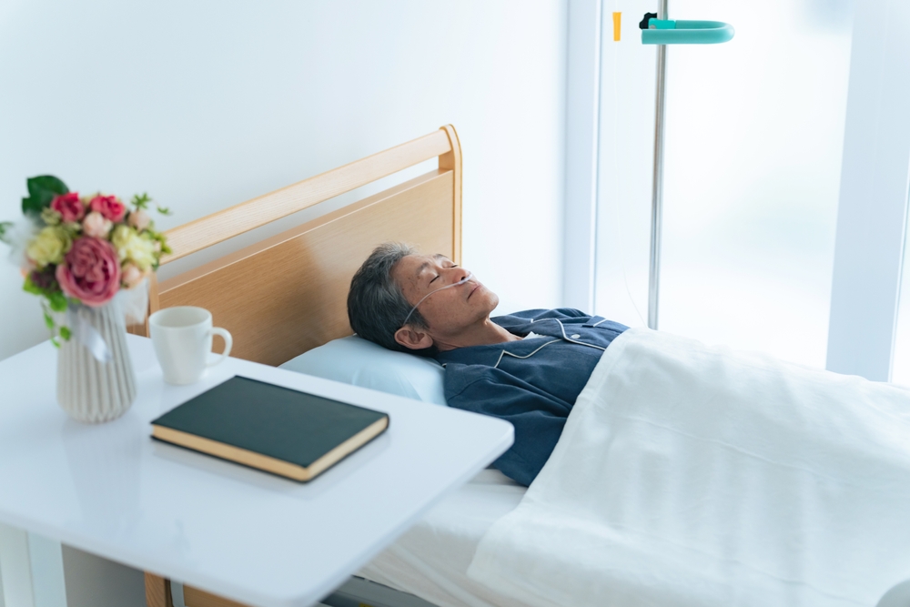 Elderly Asian man sleeping in bed with oxygen tube.