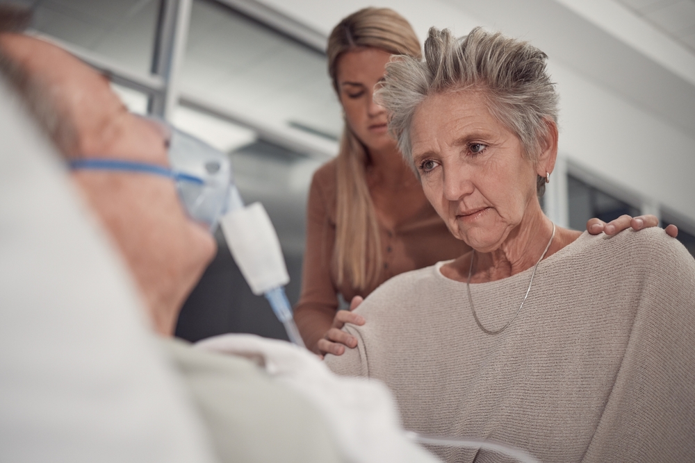 Sad family, old woman and man in bed at hospital with ventilator for breathing, healthcare or support. Senior wife, husband and deathbed with cancer in lungs at clinic, mother and daughter solidarity