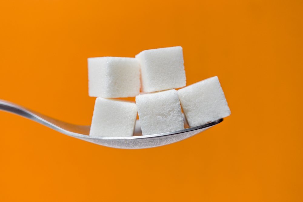 Heap of sugar cubes on a spoon against orange background