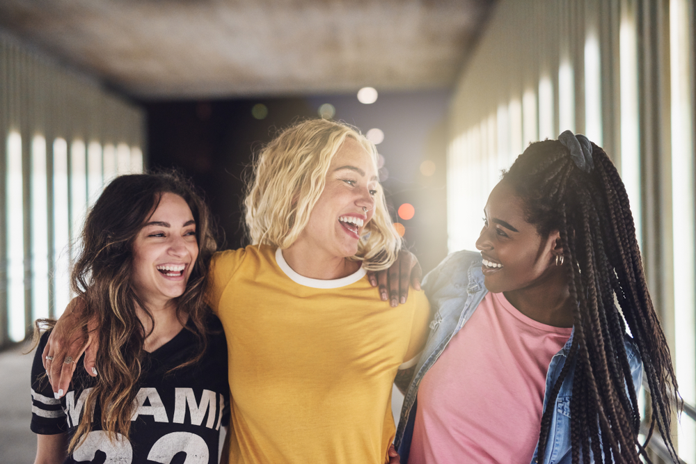 Laughing group of diverse young girlfriends having fun while walking together down a walkway in the city at night