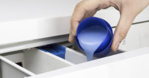 person filling laundry machine with detergent