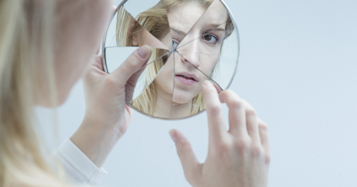 person looking at self in broken mirror