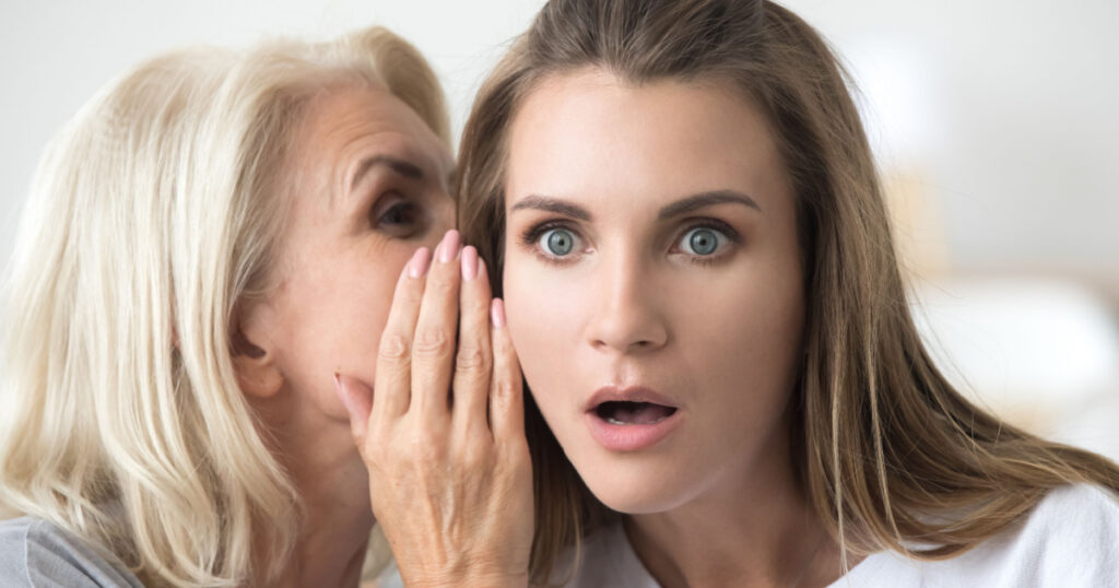 Old mother whispering in ear of adult daughter telling secret or unbelievable news, older and young women gossiping, shocked lady surprised by hearing latest rumors chatting with female aged friend