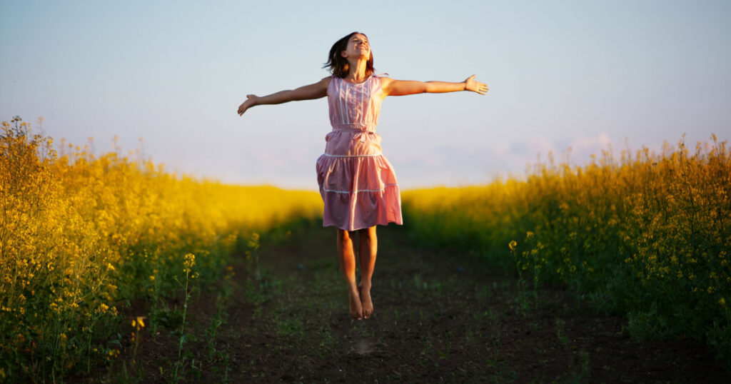 Happy woman jumps to the sky in the yellow meadow at the sunset