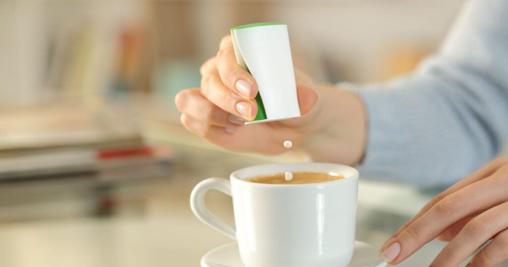 Close up of woman hand throwing saccharin pills on coffee cup on a desk at home