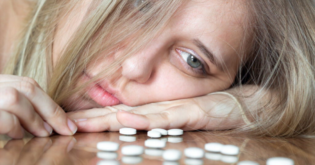 A young caucasian beautiful upset blonde woman puts her head on the table and looks at the antidepressants. Despair, apathy, depression, frustration, exhaustion, thoughts of suicide, mental disorder
