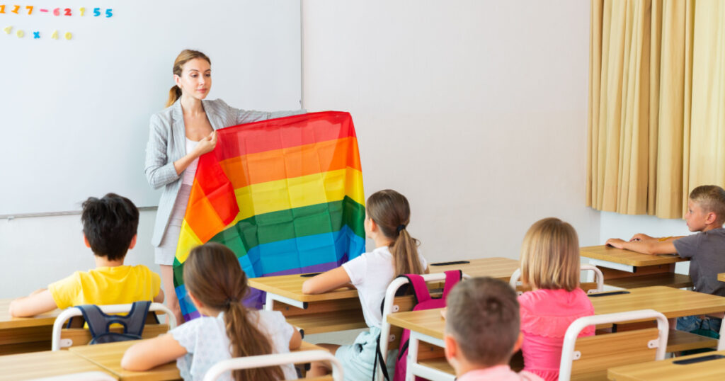 Young smiling woman teacher explaining lgbt theme to children during class in primary school