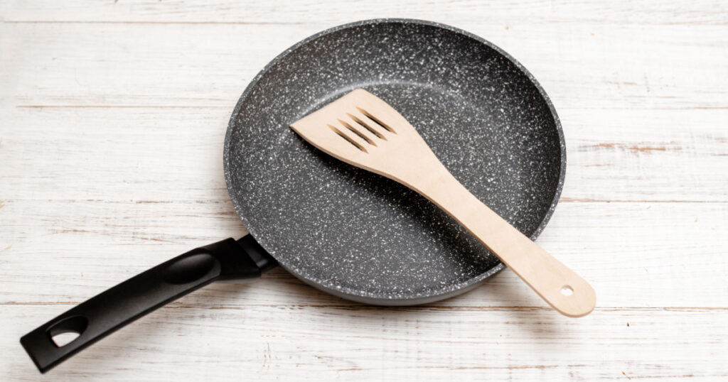 Frying pan with non-stick ceramic coating and spatula on a white wooden background. Cooking without sticking or oil.