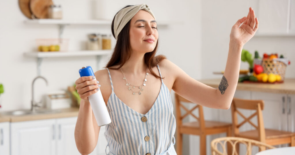 Young woman with air freshener in kitchen