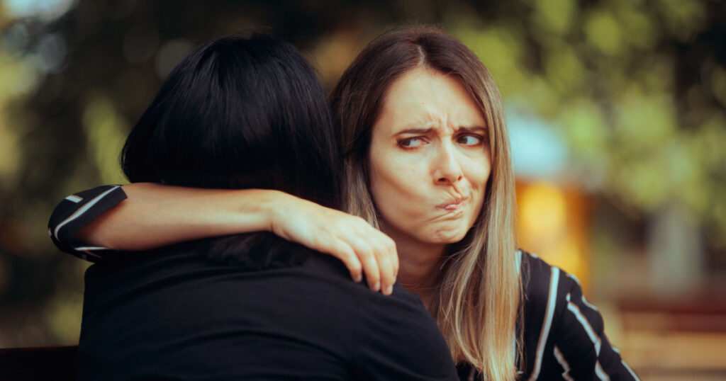 Woman Hugs Fake Friend Making Faces Behind her Back Backstabbing toxic girlfriend embracing someone with bad intentions