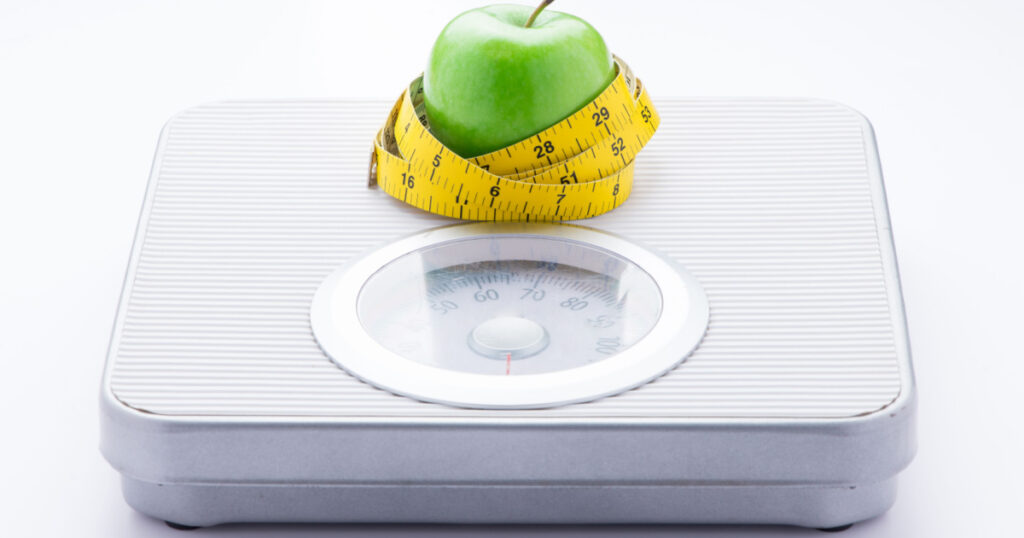 concept of eating healthy and maintaining good body. Apple and tape measure on bathroom scale isolated on white background.