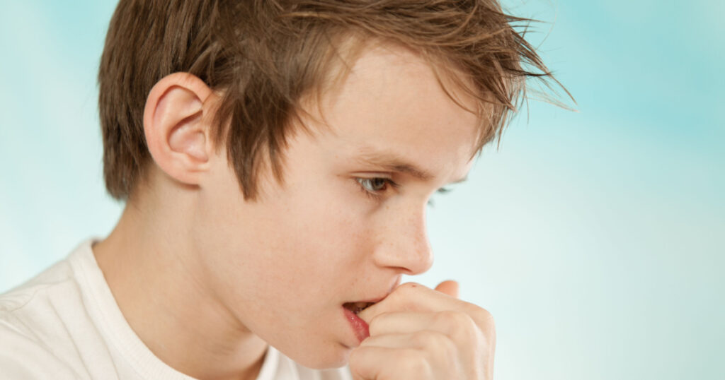 Thoughtful worried young boy biting his nails in trepidation as he stares at the ground with a serious expression, profile head shot on blue with copy space