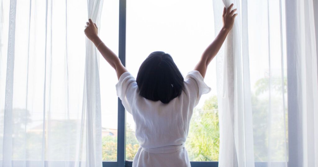 Woman, wake up and open the curtains in the morning to get fresh air.