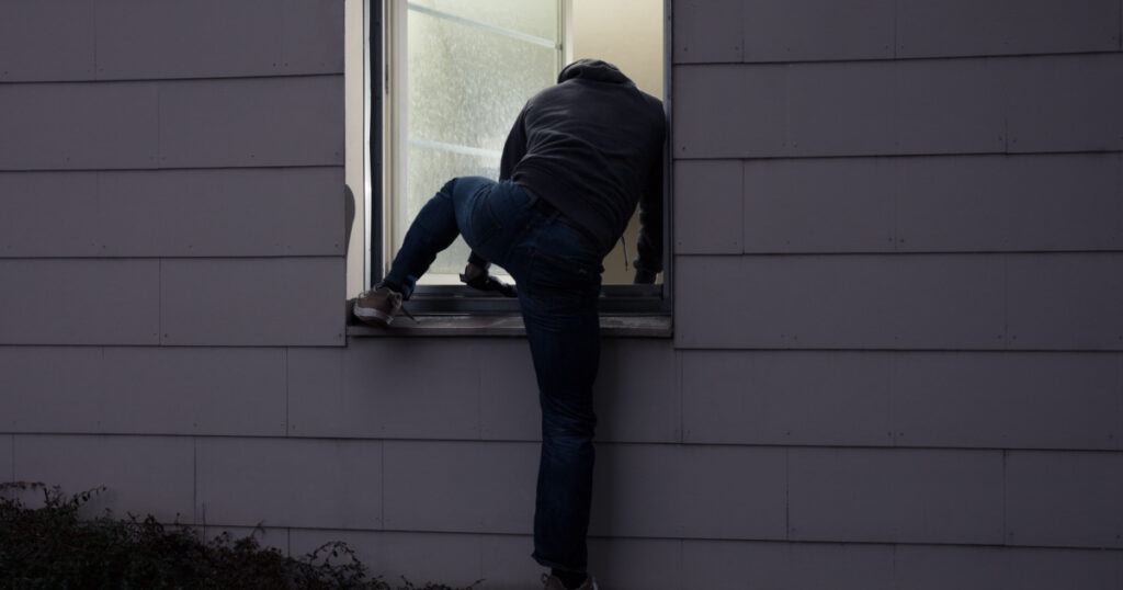 Rear View Of A Burglar Entering In A House Through A Window