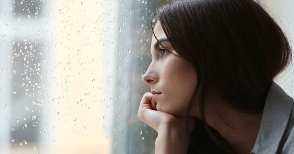 Depressed young woman near window at home, closeup
