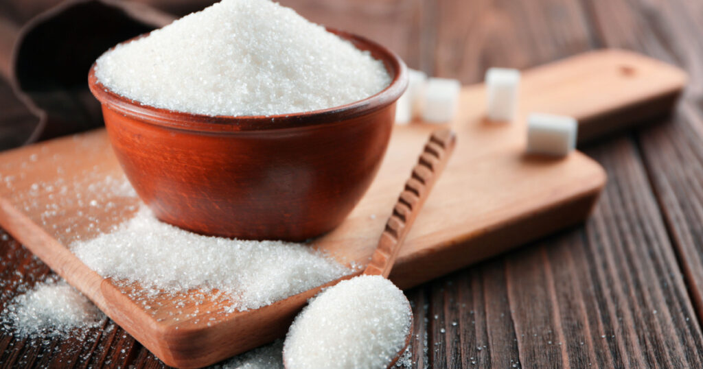 Bowl and spoon full of sugar on wooden background