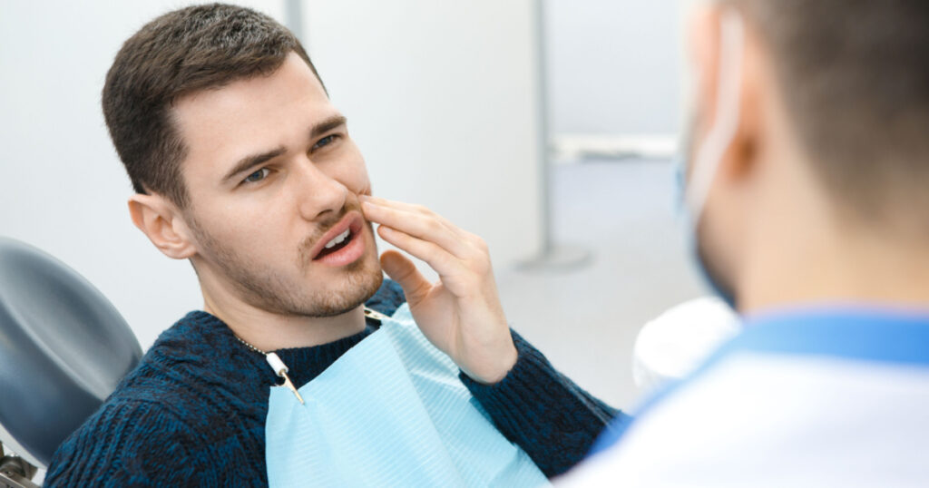 Handsome young man having toothache sitting in a dental chair. Professional dentist helping his male patient in pain copyspace painful treatment curing cure help advice painful dentistry medical