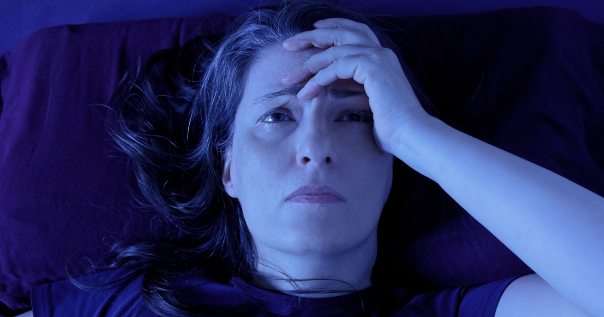 Middle aged woman lying awake in her bed at night because of insomnia, stress, fears, nightmares or illnesses like fibromyalgia