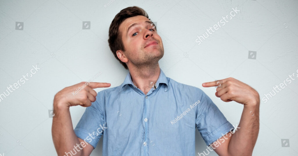 Self-satisfied and proud caucasian young man looks forward showing with index fingers on himself