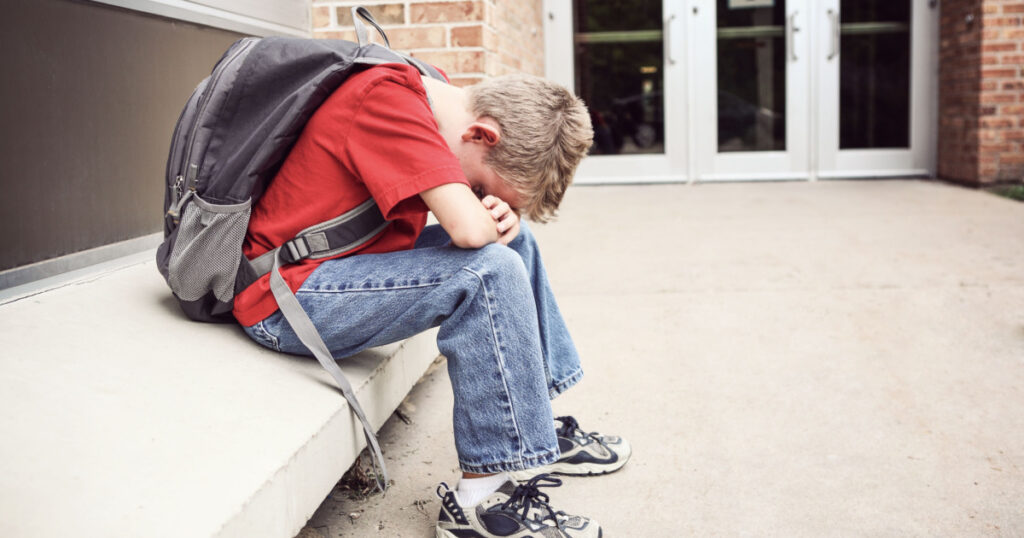 Depressed student sitting outside of school hiding his face
