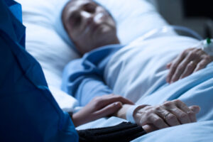 Multiple Indicators of Fraud Found in Hundreds of LA Hospices Sick woman dying in a hospital bed and her family praying for her health