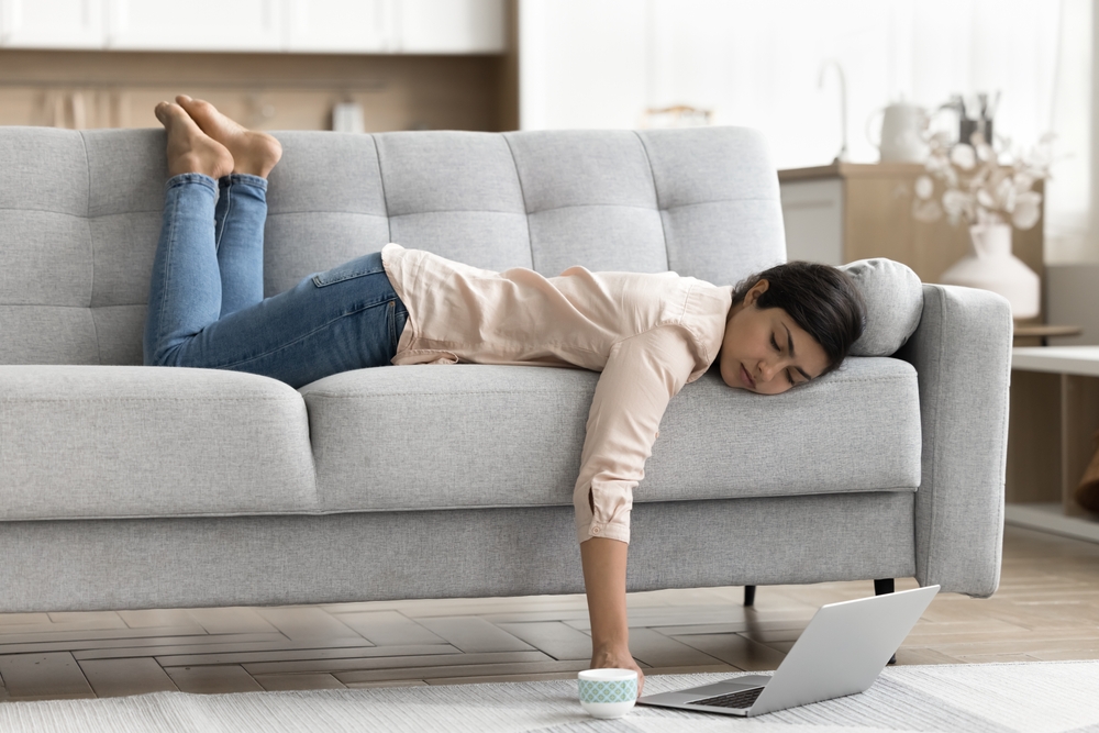 Young Indian woman working or studying on laptop, feel exhausted, without energy or motivation looks overworked fell asleep lying on sofa. Boring weekend alone at home, procrastination, daytime nap