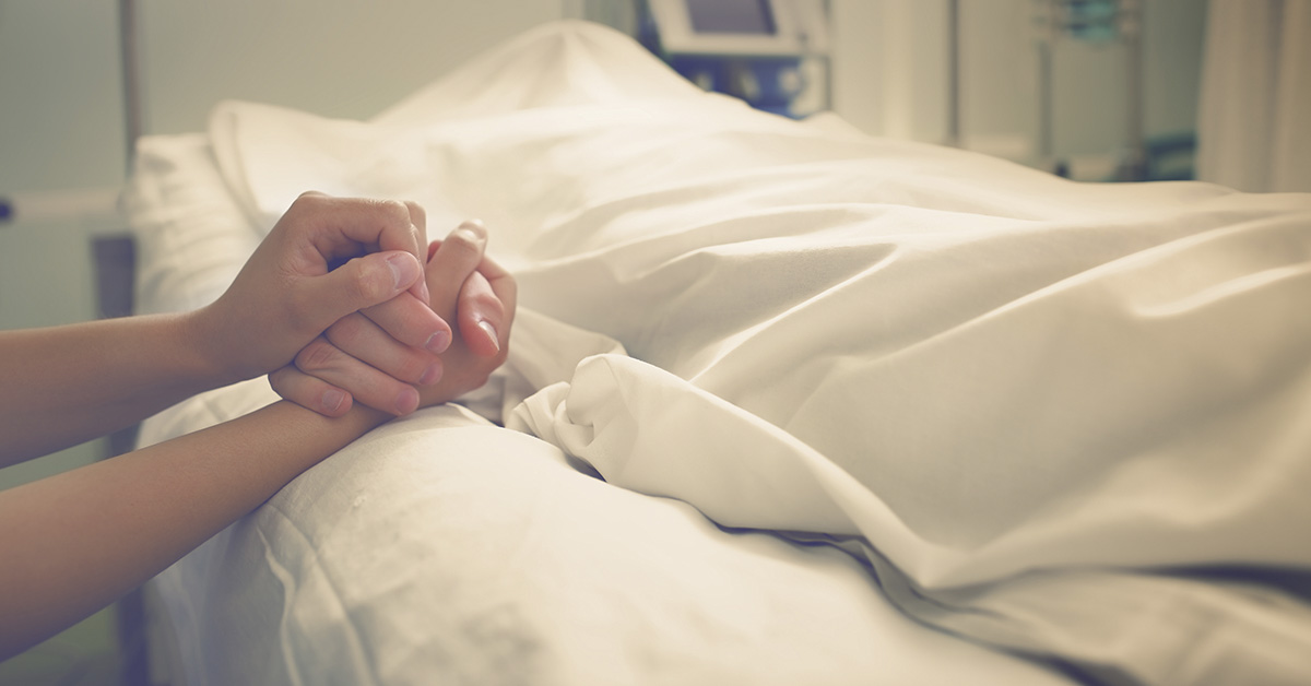 hand of patient in hospital bed being held. Hospice, end of life concept