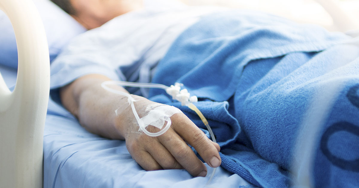 person laying in hospital bed with IV in hand