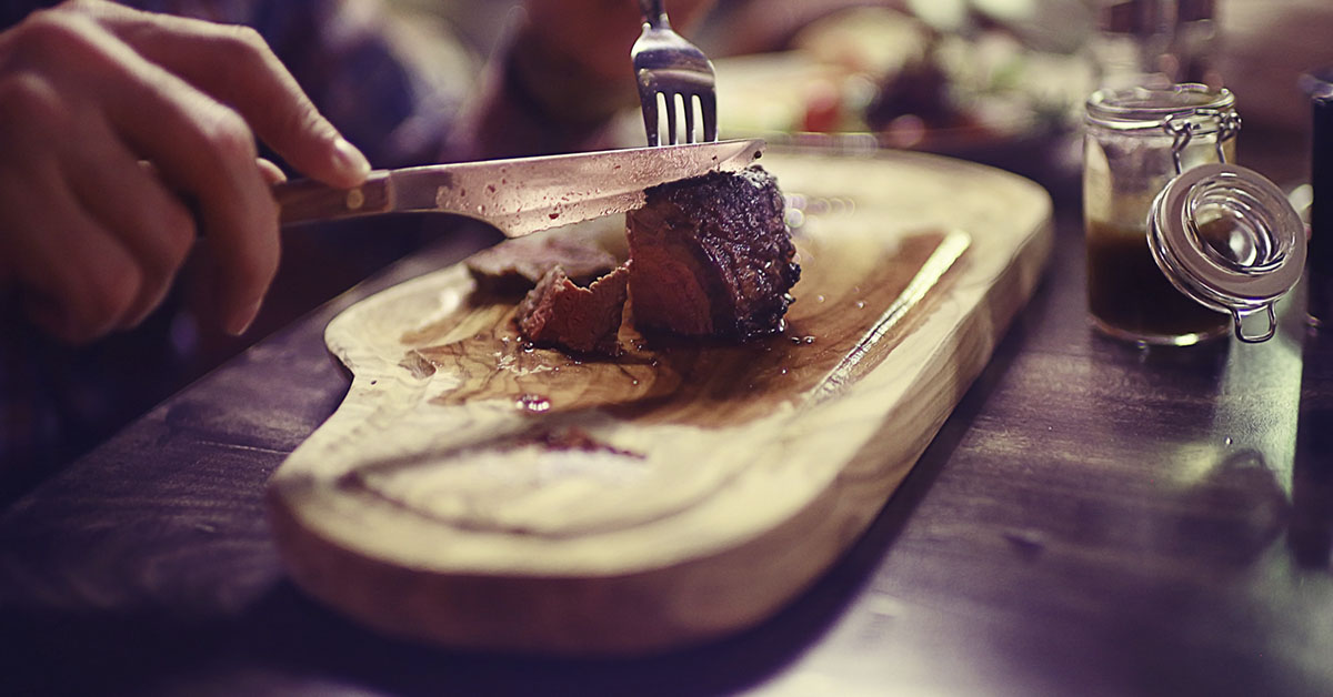 person cutting a steak on a cutting board