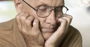 glum old man with head resting on hands. Man appears sad.