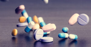 This Common Medication Could Lead to Irreversible Health Conditions various medications being dropped onto surface. Pills, tablets, capsules.
