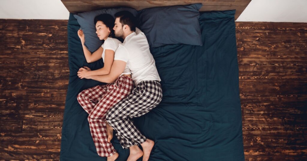 Top view. Young couple in pajamas sleeps close together on bed at home. Sleep poses. Young couple of people are at domestic atmosphere. Couple's sleep concept.