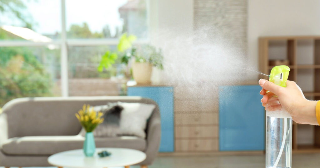 Woman spraying air freshener at home