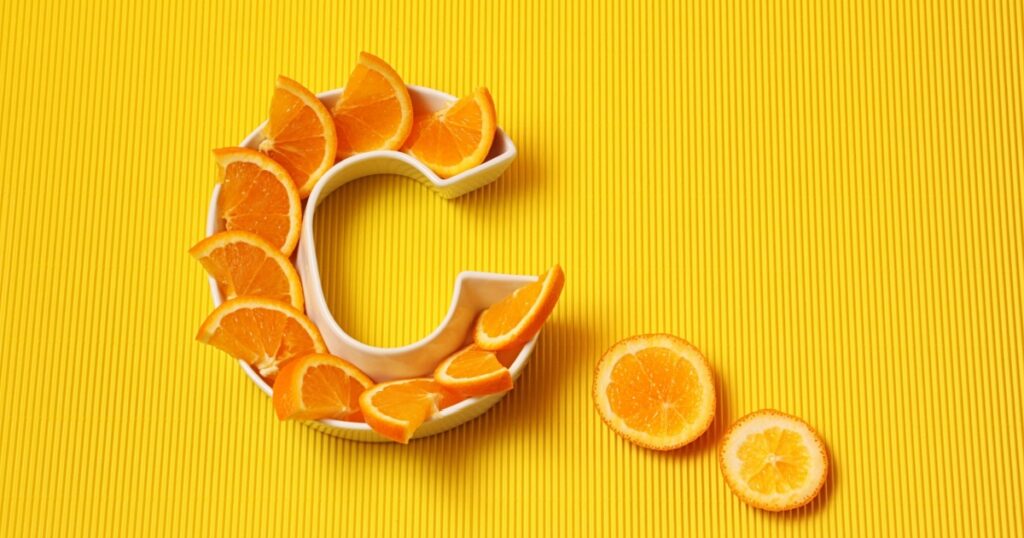Vitamin C in food concept. Plate in shape of letter C with orange slices on bright yellow background. Ascorbic acid is important for immune system function.
