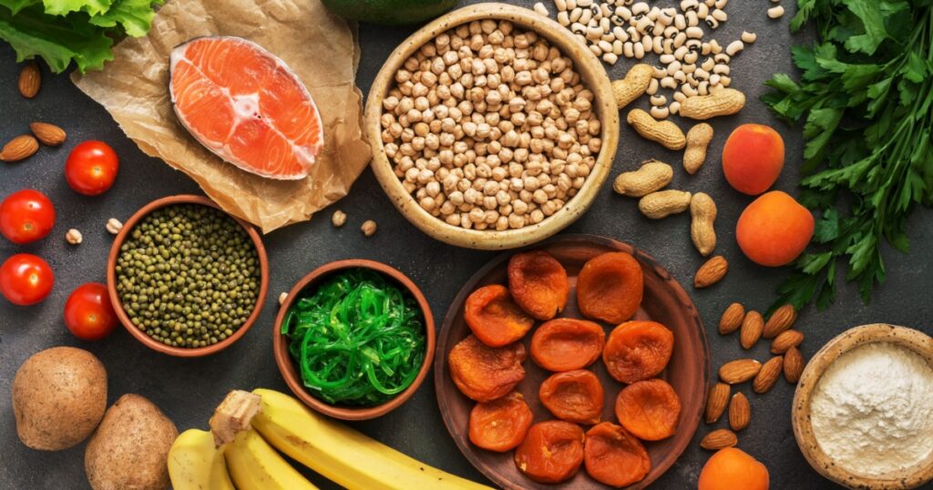 Healthy foods high in potassium. A variety of legumes, salmon, fruits, vegetables, dried apricots, seaweed chuka and nuts on a dark background. Top view, flat lay
